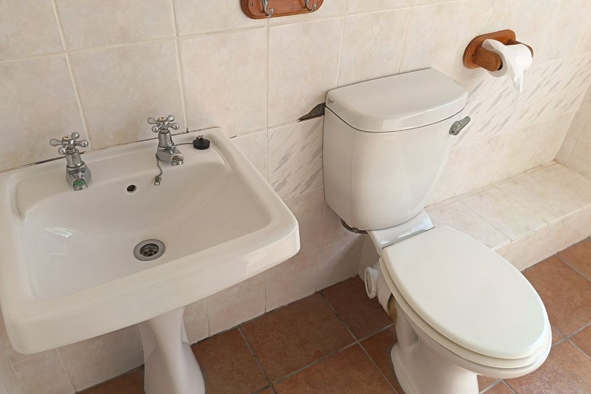 A functional bathroom featuring a pedestal basin and ceramic toilet with neutral wall and floor tiling.