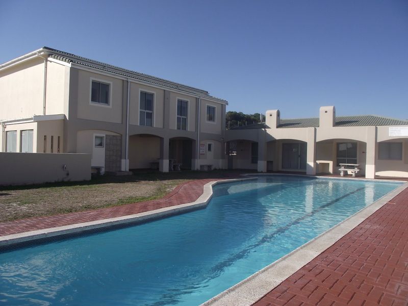 A communal swimming pool area featuring a paved deck, covered patio spaces, and multi-story apartment building exterior.