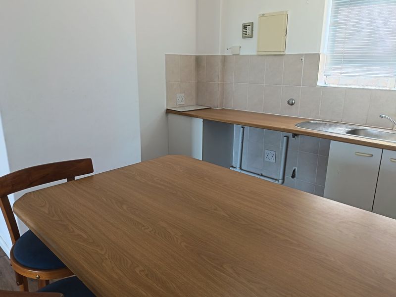 A functional kitchen area featuring a stainless steel sink, tiled backsplash, and laminate countertops, currently requiring cabinet repairs and plumbing concealment.
