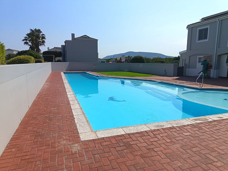A well-maintained outdoor swimming pool area featuring brick paving, a surrounding boundary wall, and integrated pool steps.