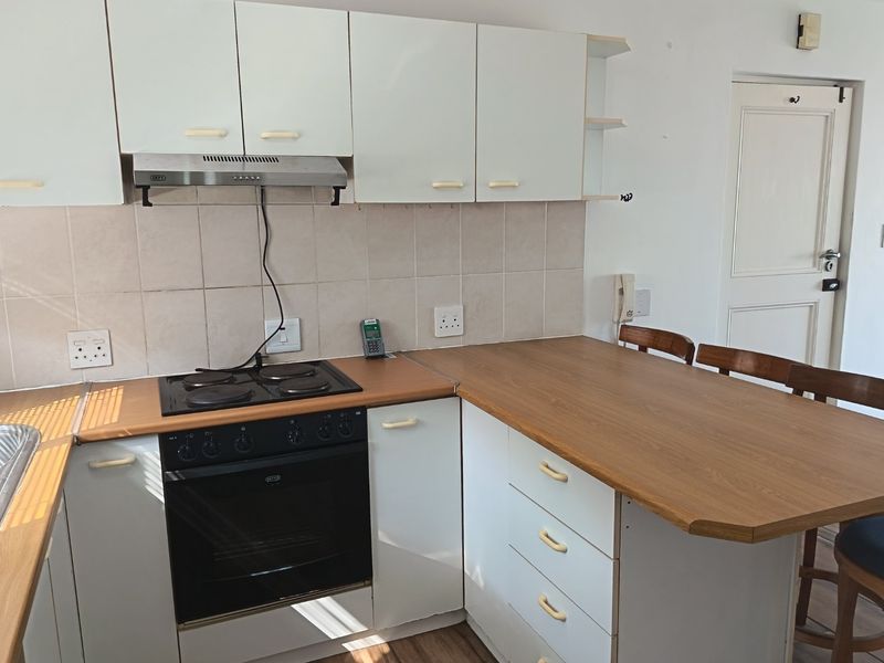 Functional kitchen featuring white cabinetry, wood-look laminate countertops, built-in oven, electric hob, and a tiled backsplash with an integrated breakfast bar area.