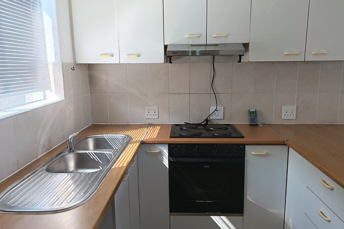 A functional kitchen featuring white cabinetry, laminate countertops, a double bowl stainless steel sink, and a built-in electric oven with a hob and extractor.