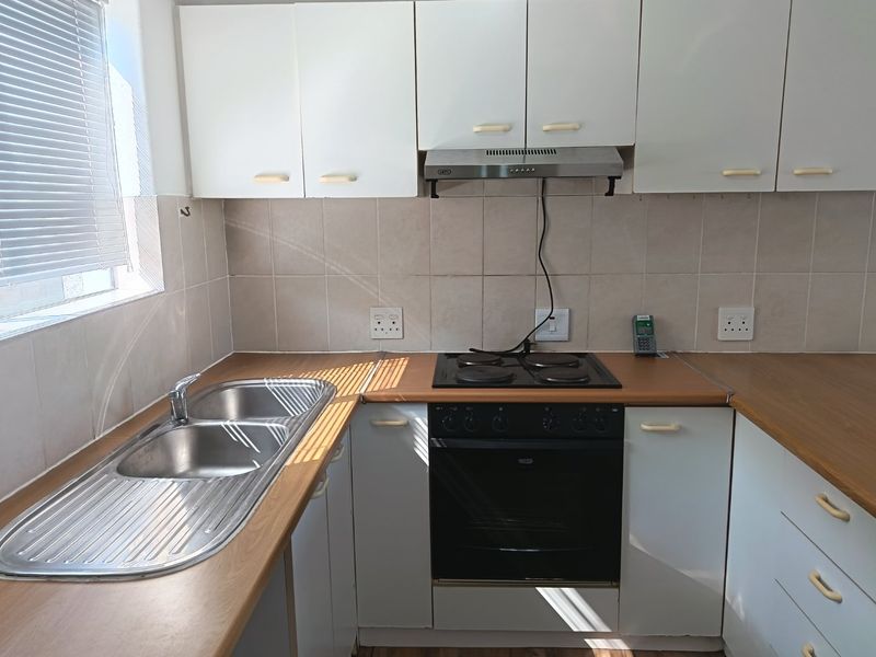 A functional kitchen featuring white cabinetry, laminate countertops, a double bowl stainless steel sink, and a built-in electric oven with a hob and extractor.
