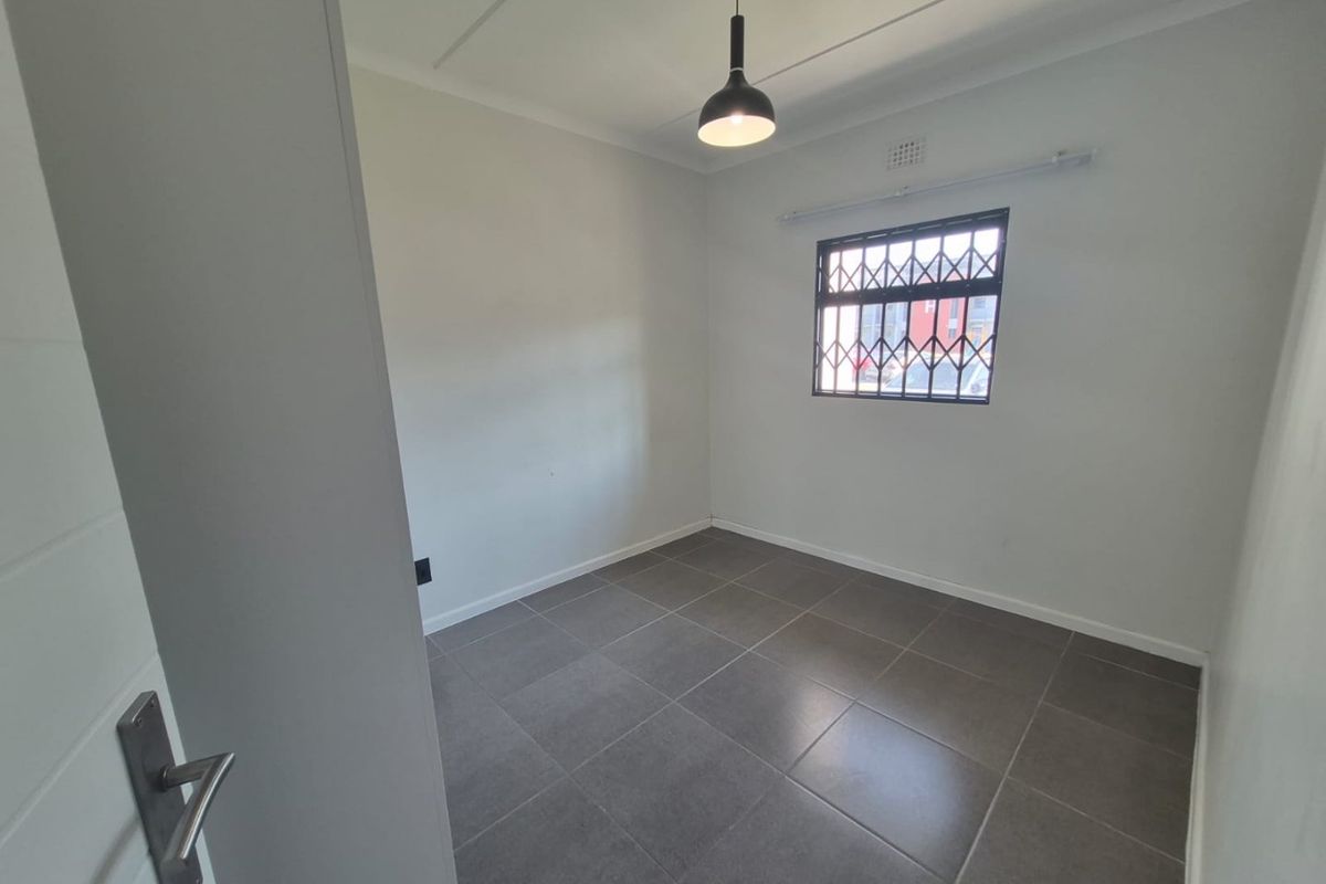 A clean, empty bedroom featuring neutral tiled flooring, a modern pendant light, and a window fitted with a security gate.