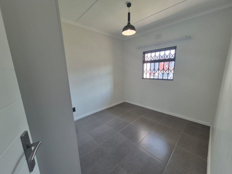 A clean, empty bedroom featuring neutral tiled flooring, a modern pendant light, and a window fitted with a security gate.