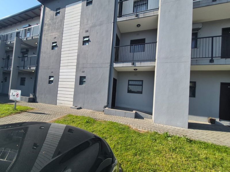 Exterior view of a modern apartment complex featuring grey rendered facades, paved walkways, and private balconies with metal railings.