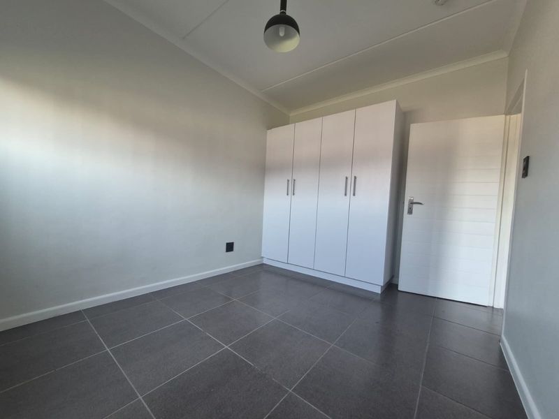 A clean, empty bedroom featuring modern grey floor tiles and white built-in cupboards, providing a neutral canvas for personalization.