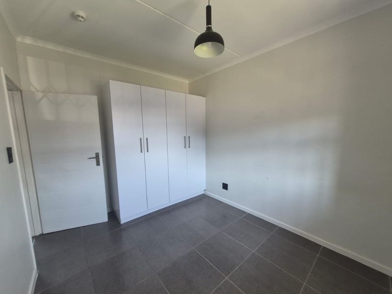 A clean, empty bedroom featuring modern grey floor tiles, white walls, and built-in white cupboards, providing a neutral canvas for personalization.