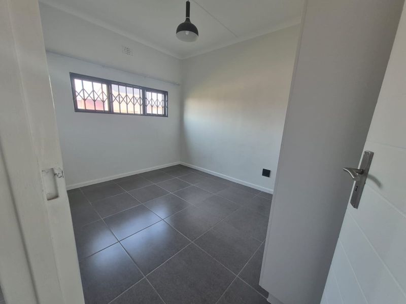 A clean, empty bedroom featuring neutral grey floor tiles, a pendant light fixture, and a window fitted with security bars.
