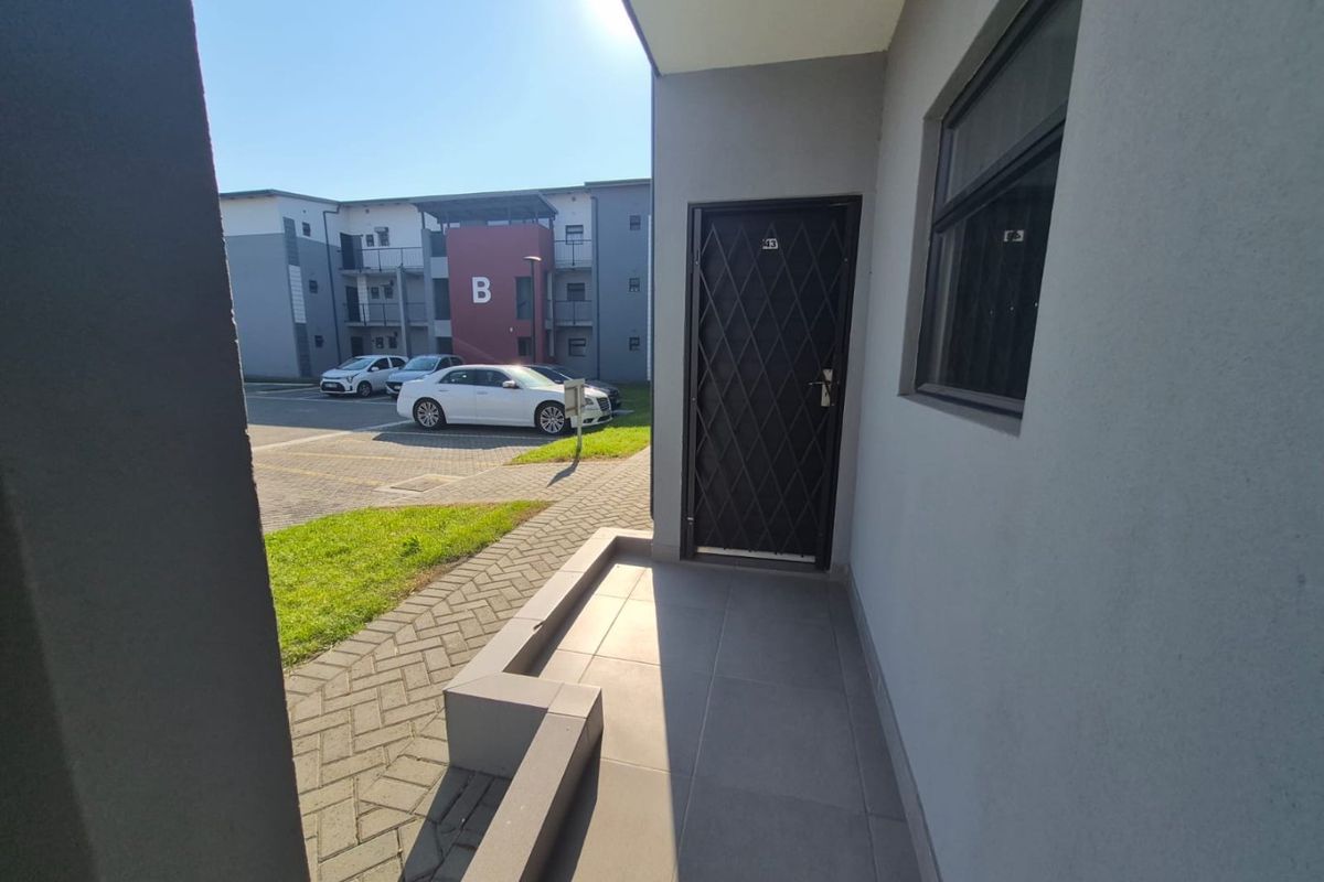 A clean, modern apartment entrance featuring a secure metal gate, tiled porch area, and paved exterior walkway.