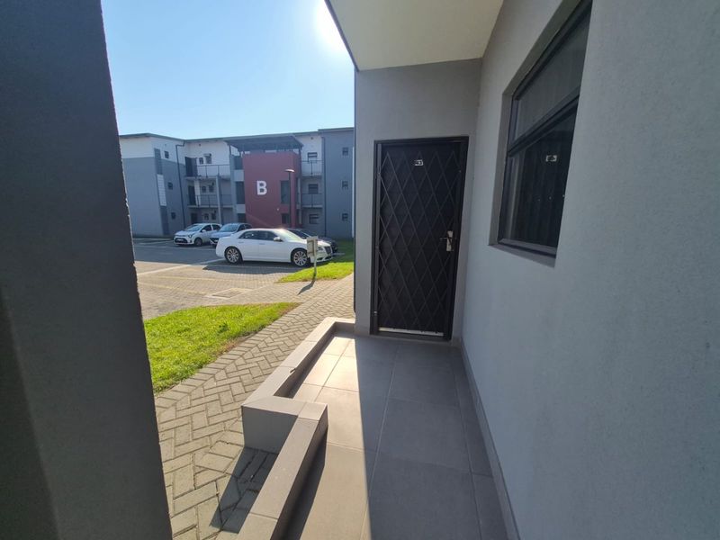 A clean, modern apartment entrance featuring a secure metal gate, tiled porch area, and paved exterior walkway.