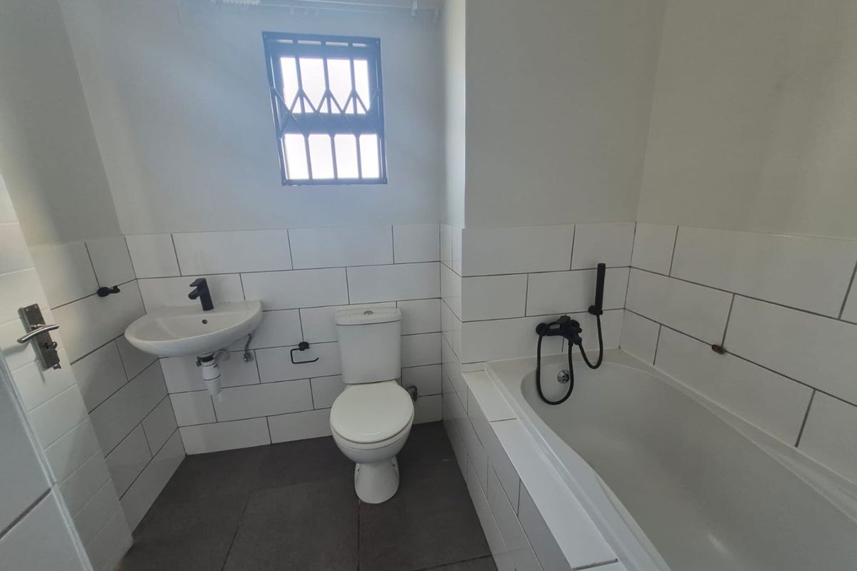 A functional bathroom featuring a wall-mounted basin, toilet, and a built-in bathtub with a handheld shower mixer, finished with white subway wall tiles.