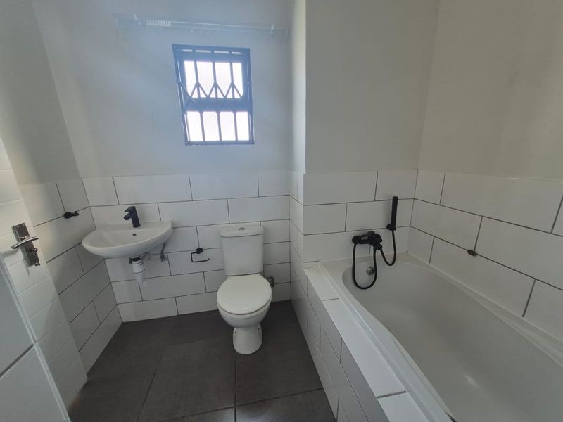 A functional bathroom featuring a wall-mounted basin, toilet, and a built-in bathtub with a handheld shower mixer, finished with white subway wall tiles.