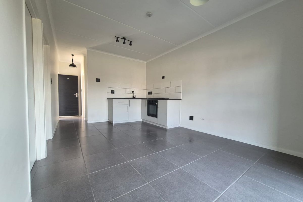 An open-plan living and kitchen area featuring modern grey floor tiles, white cabinetry, a built-in oven, and a clean subway tile backsplash.
