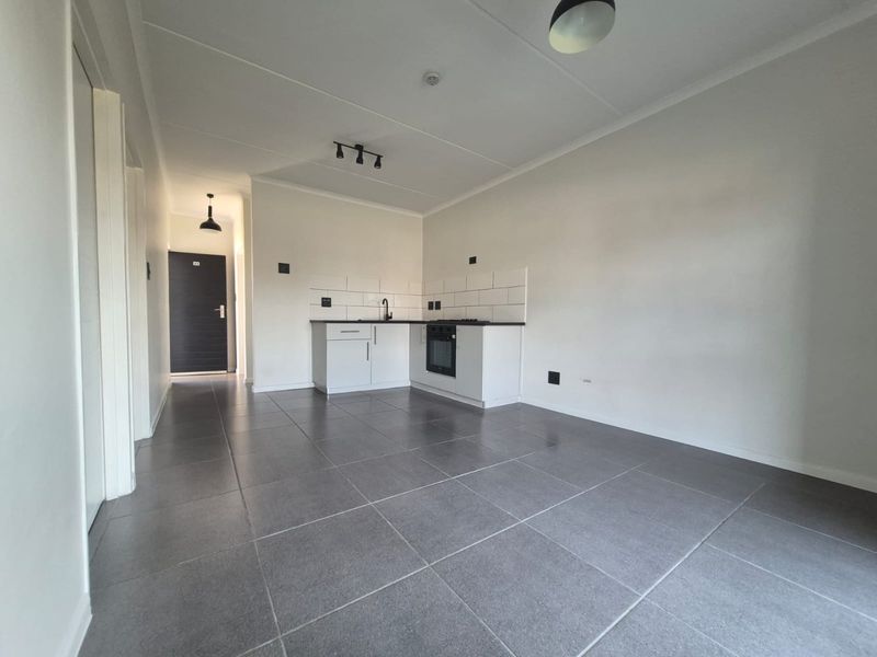 An open-plan living and kitchen area featuring modern grey floor tiles, white cabinetry, a built-in oven, and a clean subway tile backsplash.