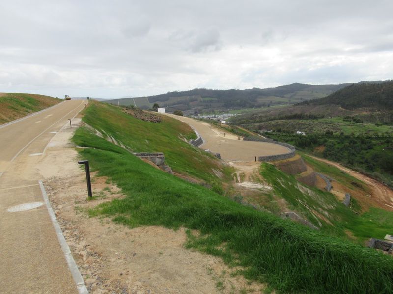 An elevated view of a residential development site featuring paved roads, landscaped embankments, and stone retaining walls overlooking a valley.