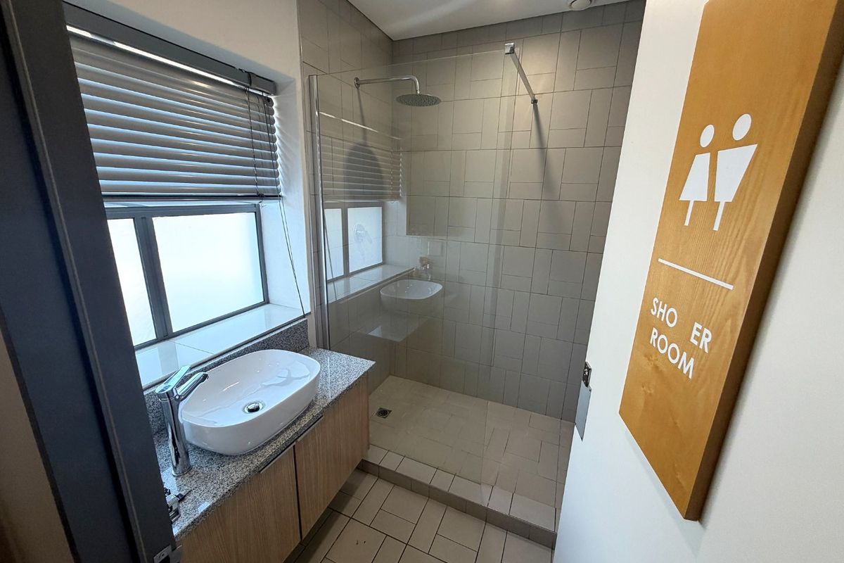Modern commercial shower room featuring a walk-in shower with rain head, granite-topped vanity with countertop basin, and neutral tiled finishes.
