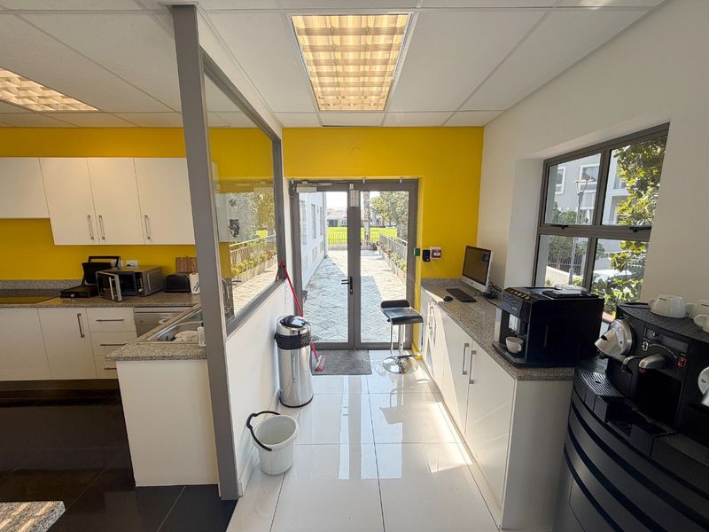 A bright commercial kitchen area featuring white cabinetry, granite countertops, tiled flooring, and direct access to an outdoor patio through double glass doors.