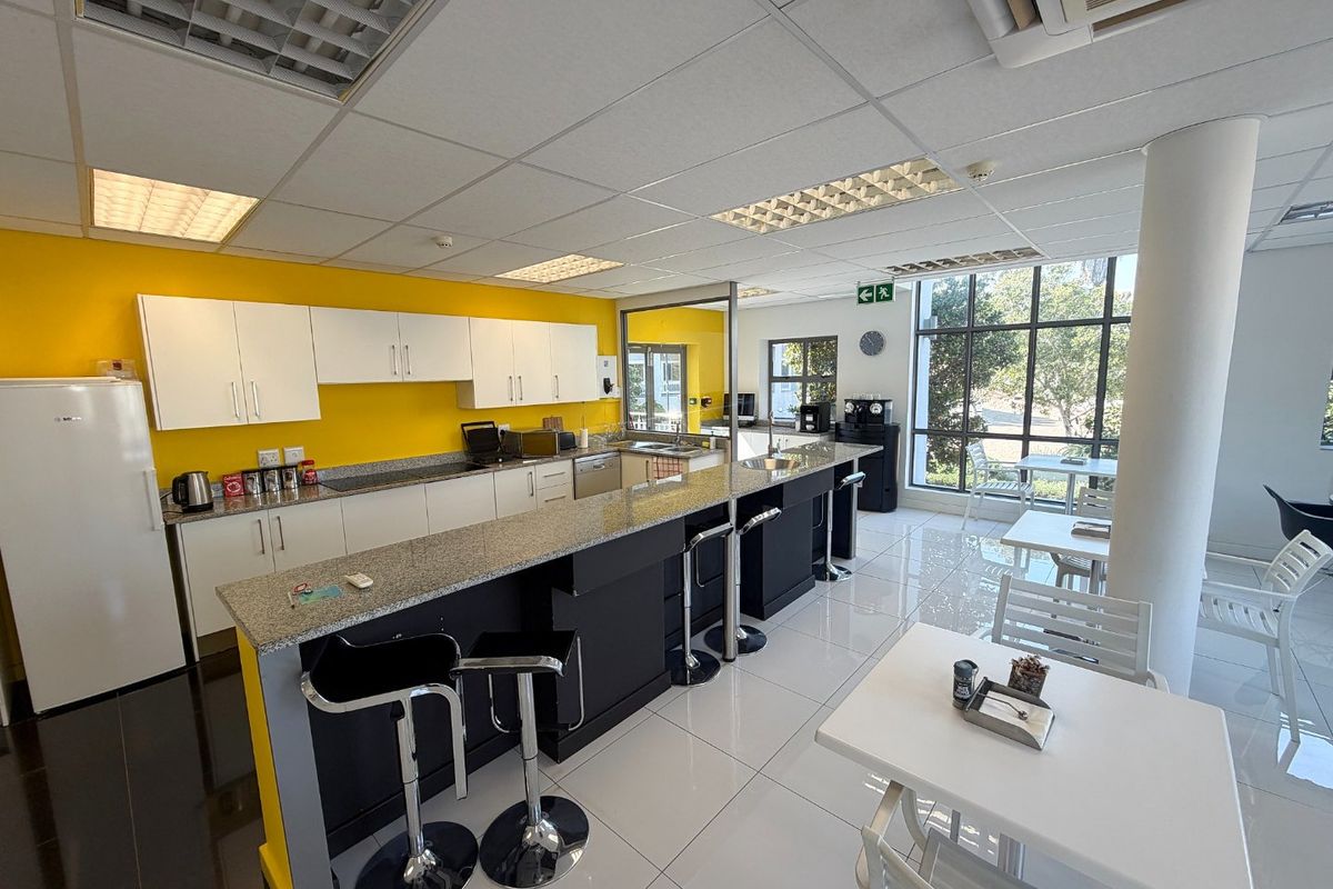 A bright commercial kitchen area featuring granite countertops, ample cabinetry, tiled flooring, and large windows providing natural light.