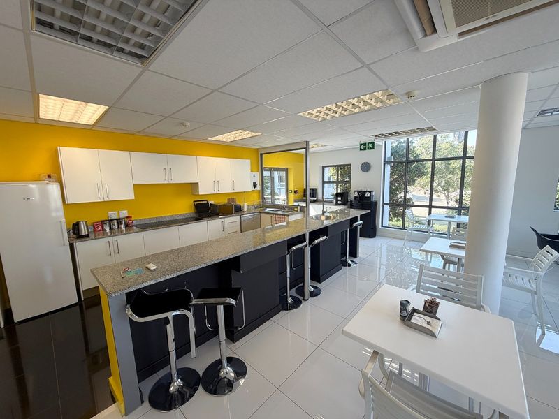 A bright commercial kitchen area featuring granite countertops, ample cabinetry, tiled flooring, and large windows providing natural light.