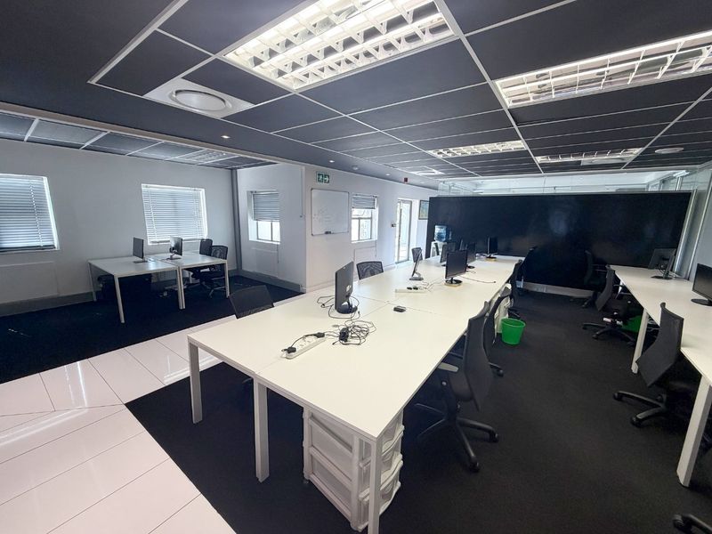 A modern open-plan commercial office space featuring a suspended ceiling, recessed lighting, and a combination of tiled and carpeted flooring.