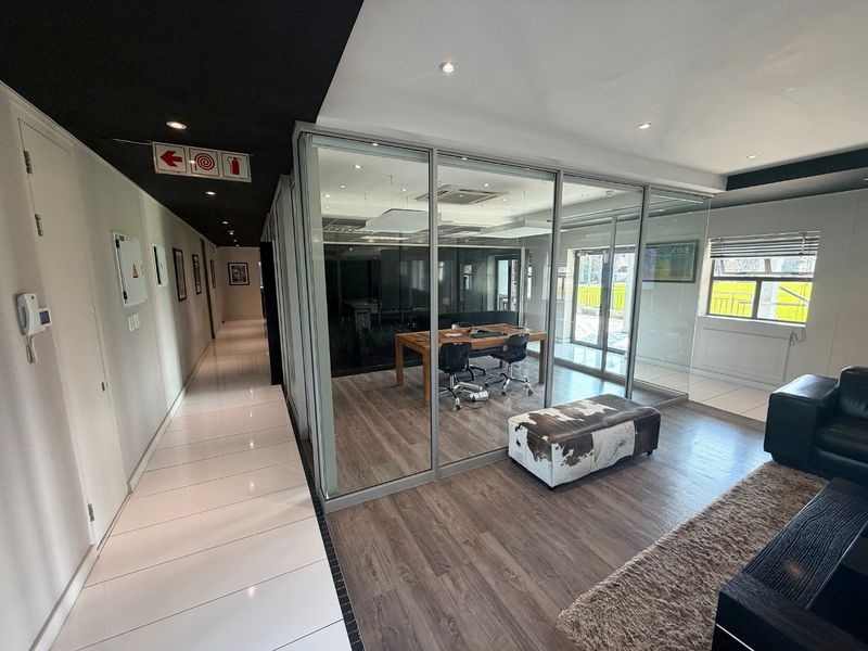 Modern commercial office space featuring glass-partitioned meeting rooms, sleek laminate and tiled flooring, and professional recessed lighting throughout the workspace.