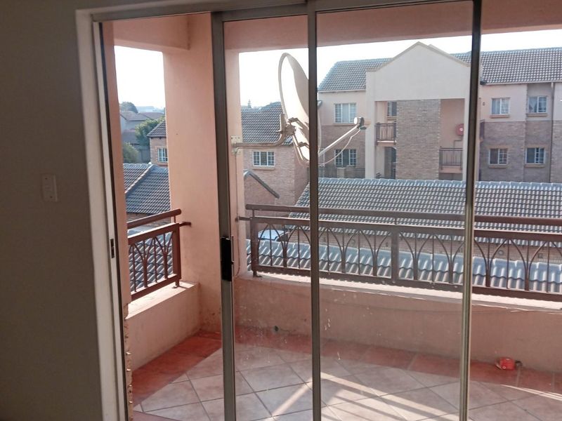 A balcony area featuring tiled flooring and a metal balustrade, accessible via a sliding glass door, overlooking the surrounding residential complex.