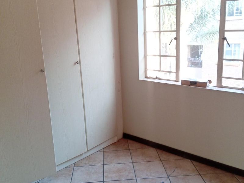 An empty bedroom featuring built-in cupboards, tiled flooring, and a window with security bars, offering a blank canvas for personalization.