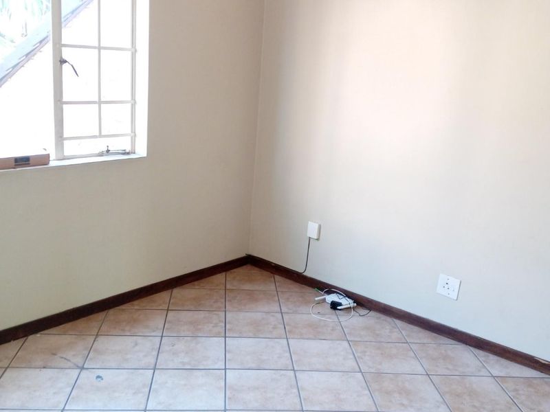 An empty bedroom featuring neutral walls, tiled flooring, and a window with security bars, providing a blank canvas for personalization.