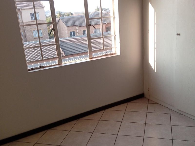 An empty bedroom featuring tiled flooring, a built-in cupboard, and a window with security bars overlooking the neighborhood.