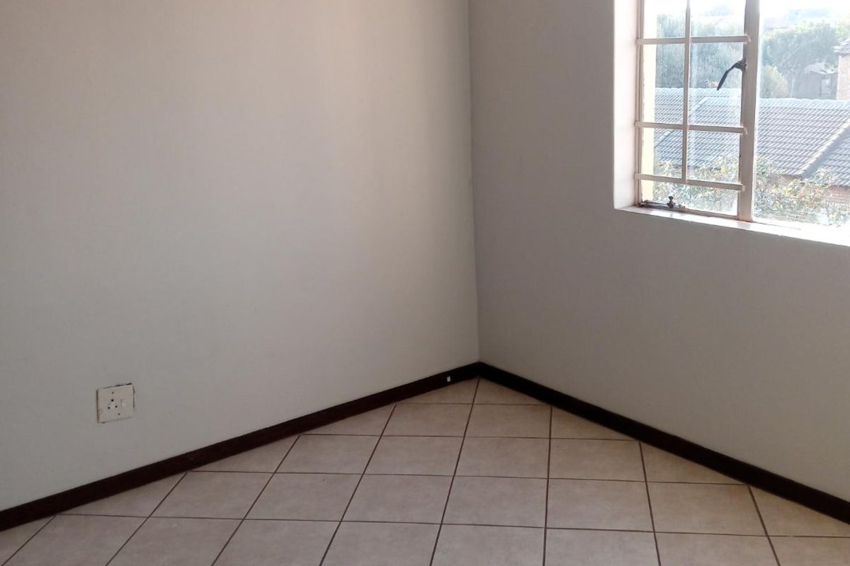An empty bedroom featuring neutral tiled flooring, clean walls, and a window with a grid pattern, providing a blank canvas for personalization.