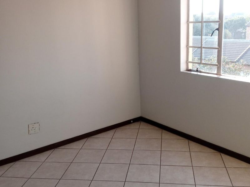 An empty bedroom featuring neutral tiled flooring, clean walls, and a window with a grid pattern, providing a blank canvas for personalization.