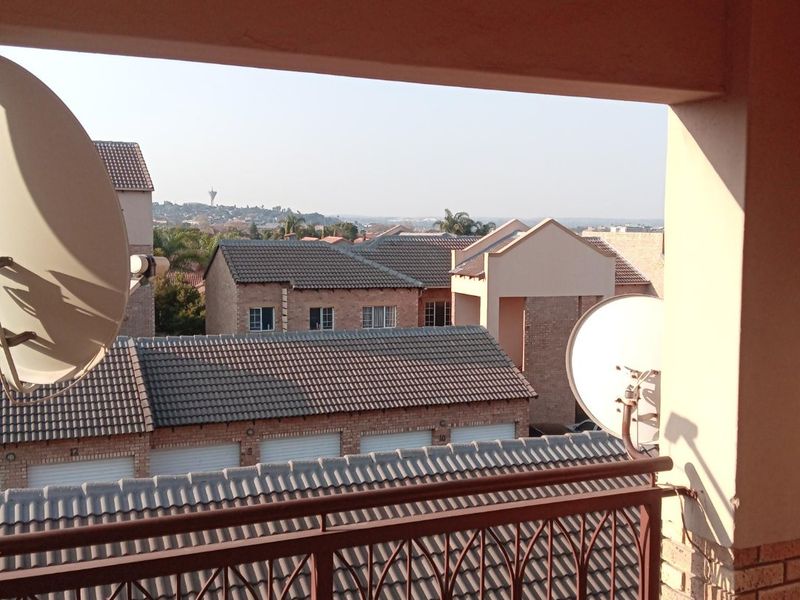 A covered balcony featuring a metal balustrade and tiled flooring, offering an elevated view over the surrounding residential complex rooftops.