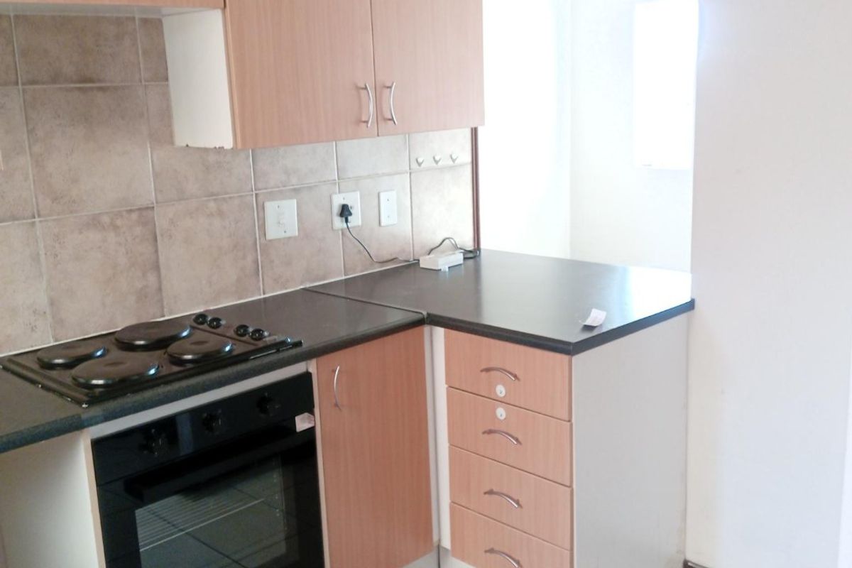 A functional kitchen featuring laminate cabinetry, built-in oven, electric hob, tiled backsplash, and ceramic floor tiles.