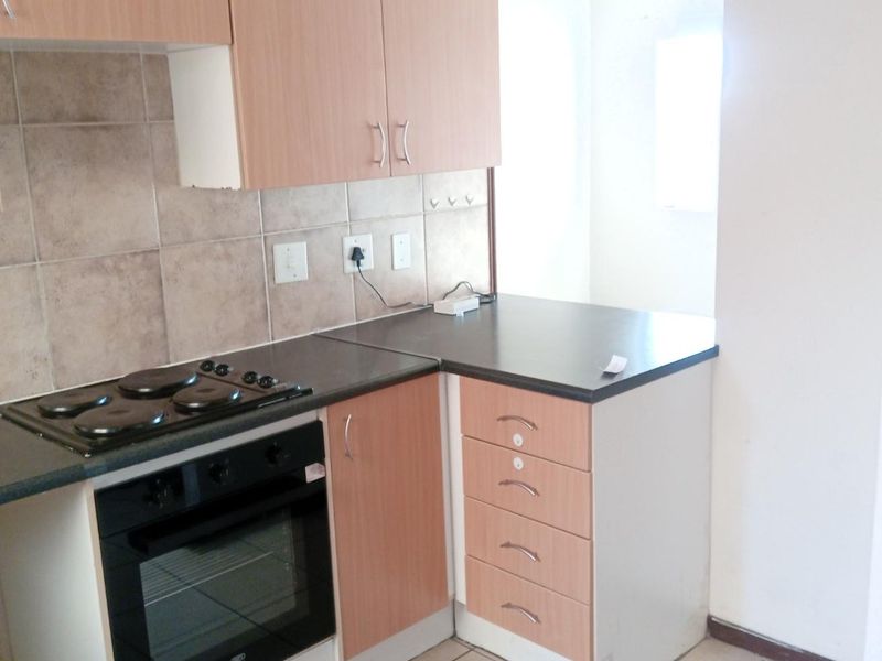 A functional kitchen featuring laminate cabinetry, built-in oven, electric hob, tiled backsplash, and ceramic floor tiles.