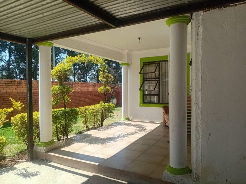 A covered patio area featuring tiled flooring and concrete columns, overlooking a private garden with a brick boundary wall.