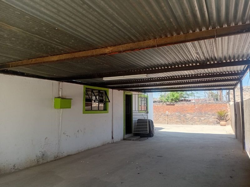 A covered outdoor parking area or garage featuring a corrugated metal roof, concrete flooring, and a secure gated entrance.