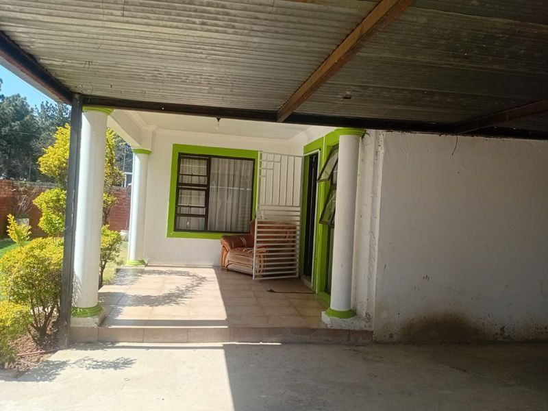 A covered patio area featuring concrete columns, tiled flooring, and a corrugated metal roof, providing a sheltered outdoor space.