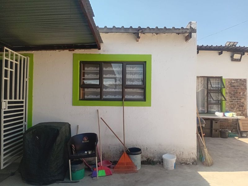 Rear exterior view of the property featuring a concrete patio area, aluminium window frames, and a corrugated metal roof structure.