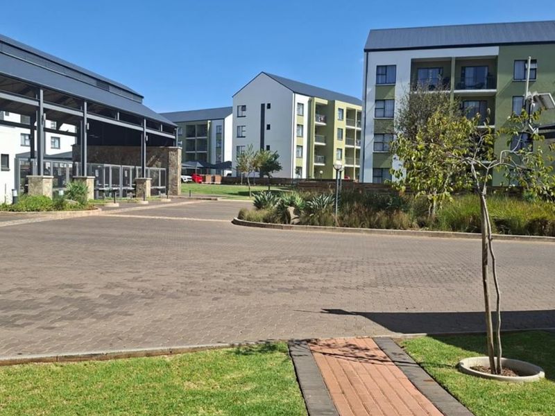 A view of the apartment complex entrance featuring paved driveways, landscaped garden areas, and modern multi-story residential buildings.