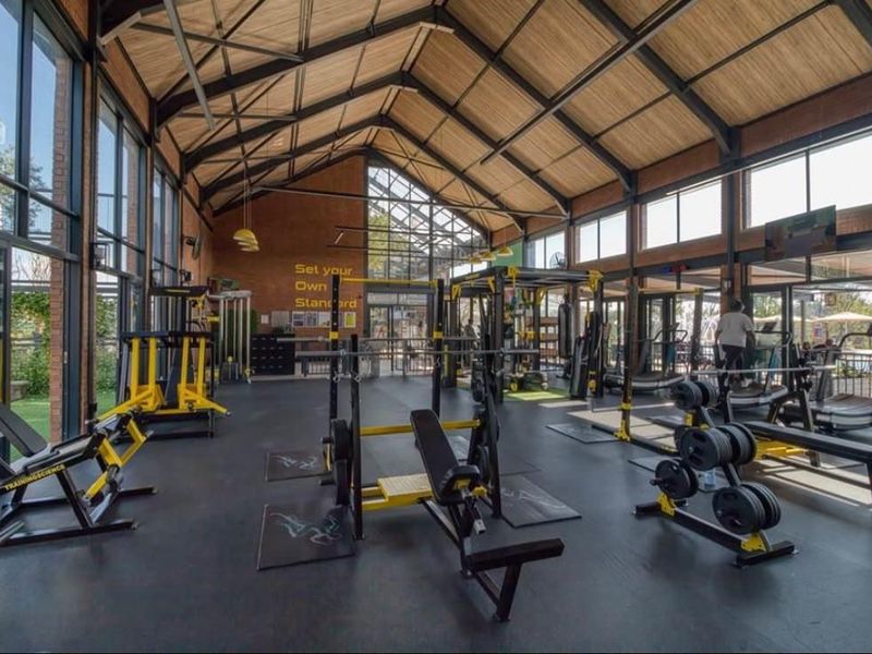 Spacious, modern gym facility featuring high vaulted ceilings with exposed steel trusses, extensive glass walls, and durable rubber flooring.