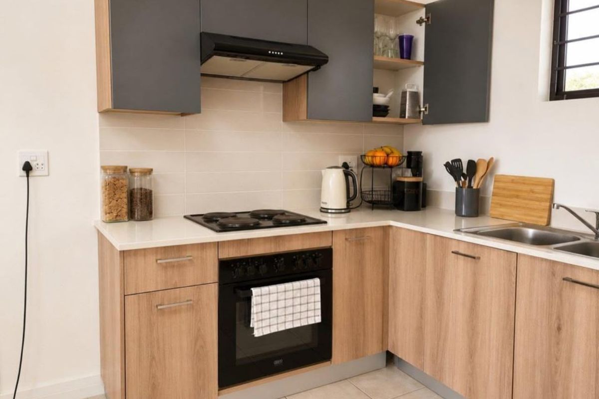 Modern kitchen featuring wood-finish cabinetry, stone-look countertops, integrated electric hob and oven, extractor fan, and a stainless steel sink with tiled backsplash.