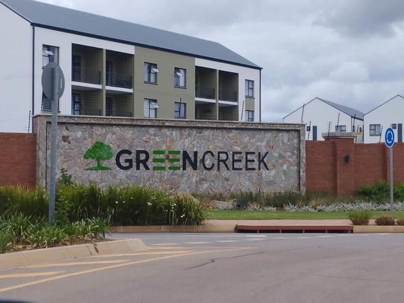 Street view of the Greencreek apartment complex entrance, featuring a stone-clad signage wall, paved access, and modern multi-story residential buildings.