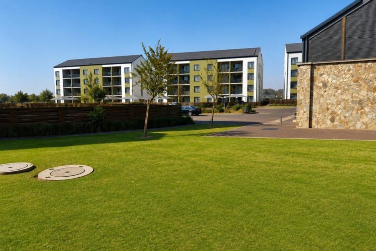 A view of the apartment complex grounds featuring well-maintained lawns, paved access areas, and modern multi-story residential buildings with balconies.