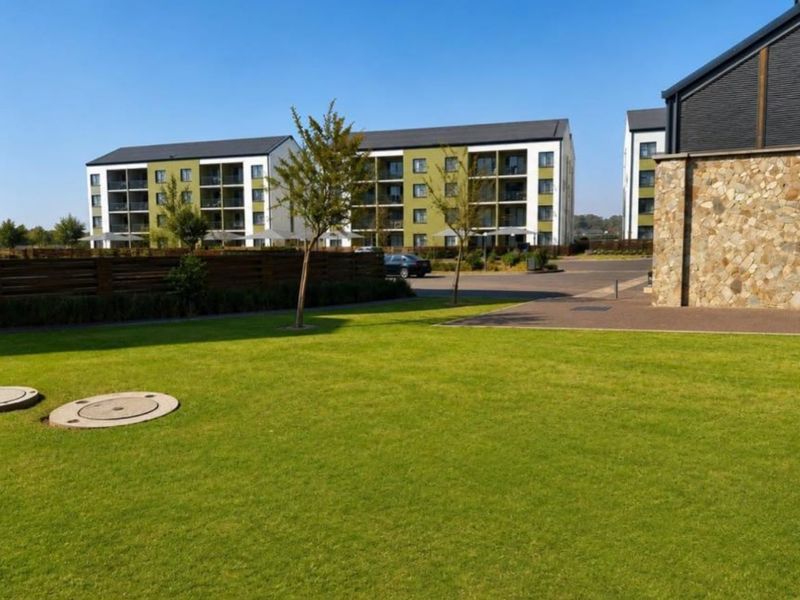 A view of the apartment complex grounds featuring well-maintained lawns, paved access areas, and modern multi-story residential buildings with balconies.