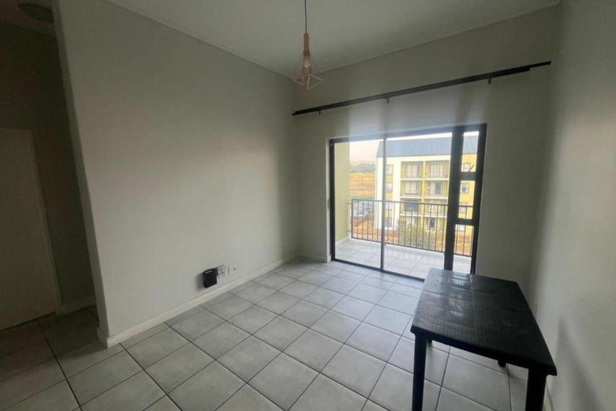 A bright, empty living area featuring neutral ceramic floor tiles, a modern pendant light, and a sliding glass door leading to a private balcony.