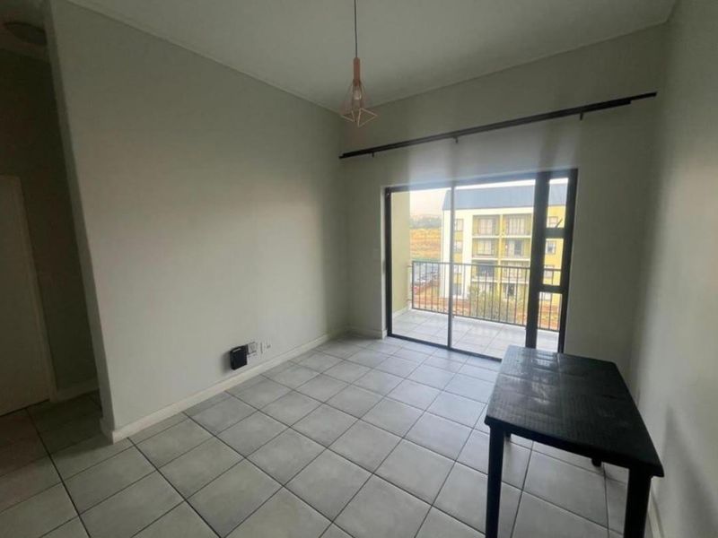 A bright, empty living area featuring neutral ceramic floor tiles, a modern pendant light, and a sliding glass door leading to a private balcony.