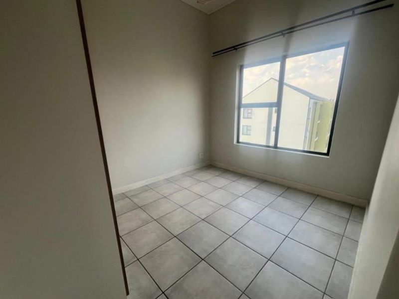 A bright, empty bedroom featuring neutral wall tones, large window with curtain rod, and clean tiled flooring throughout.
