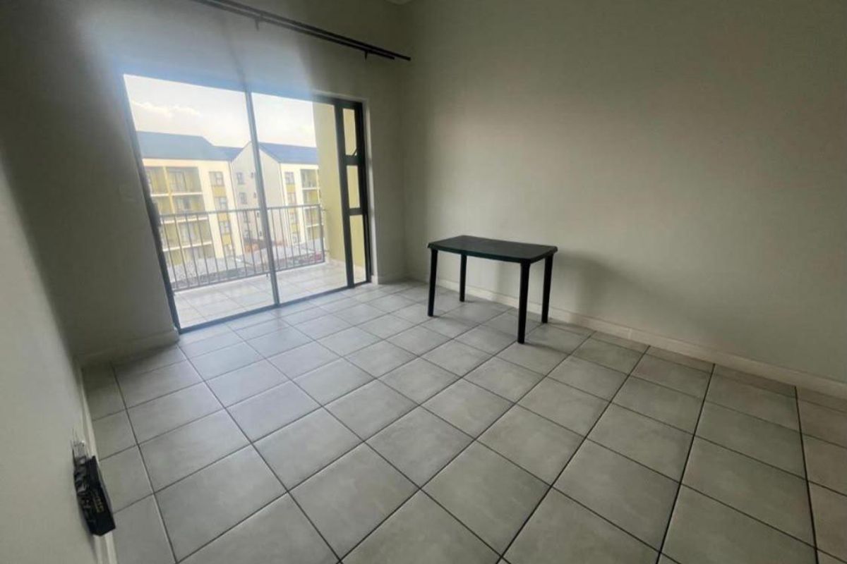 A bright, empty bedroom featuring neutral tiled flooring and a large sliding glass door providing access to a private balcony.