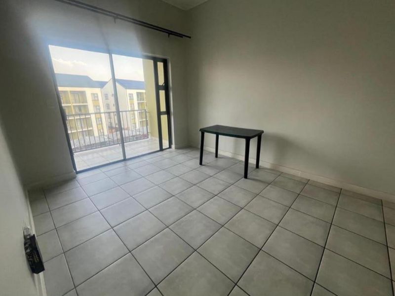 A bright, empty bedroom featuring neutral tiled flooring and a large sliding glass door providing access to a private balcony.